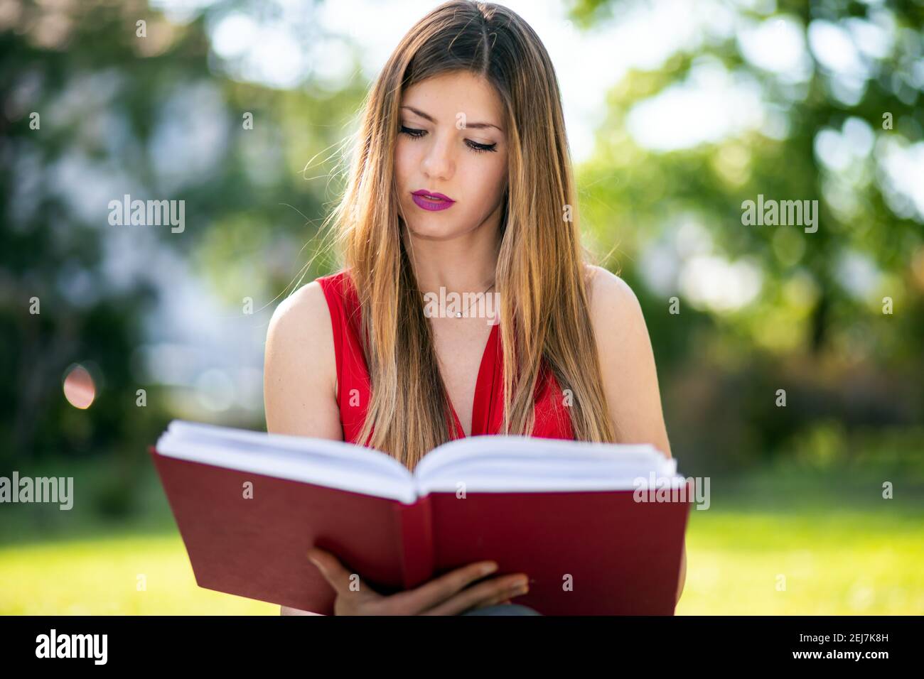 Young woman sitting in a park and reading a book Stock Photo - Alamy