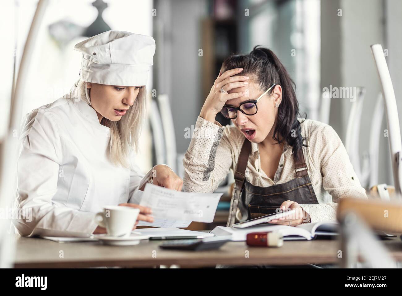 Shock over bookkeeping by female chef and restaurant owner, sitting over paperwork. Stock Photo
