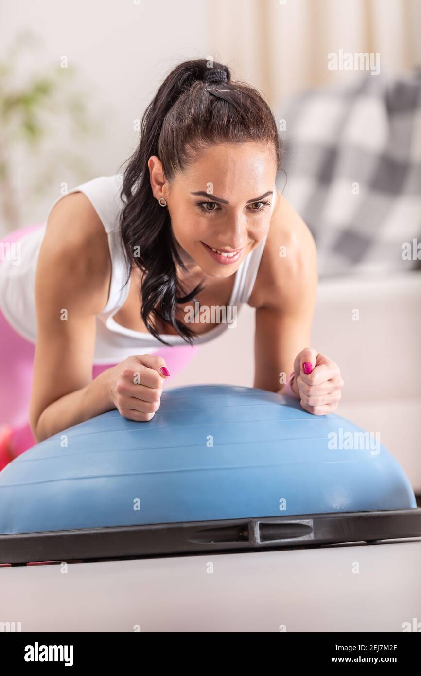 Woman focuses on holding the plank position on elbows during a home workout on a balance ball. Stock Photo