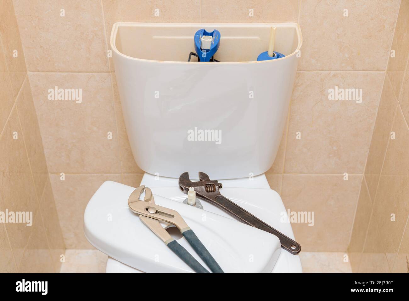 Plumbing tools in the toilet on a white toilet bowl. Drain tank cap removed Stock Photo
