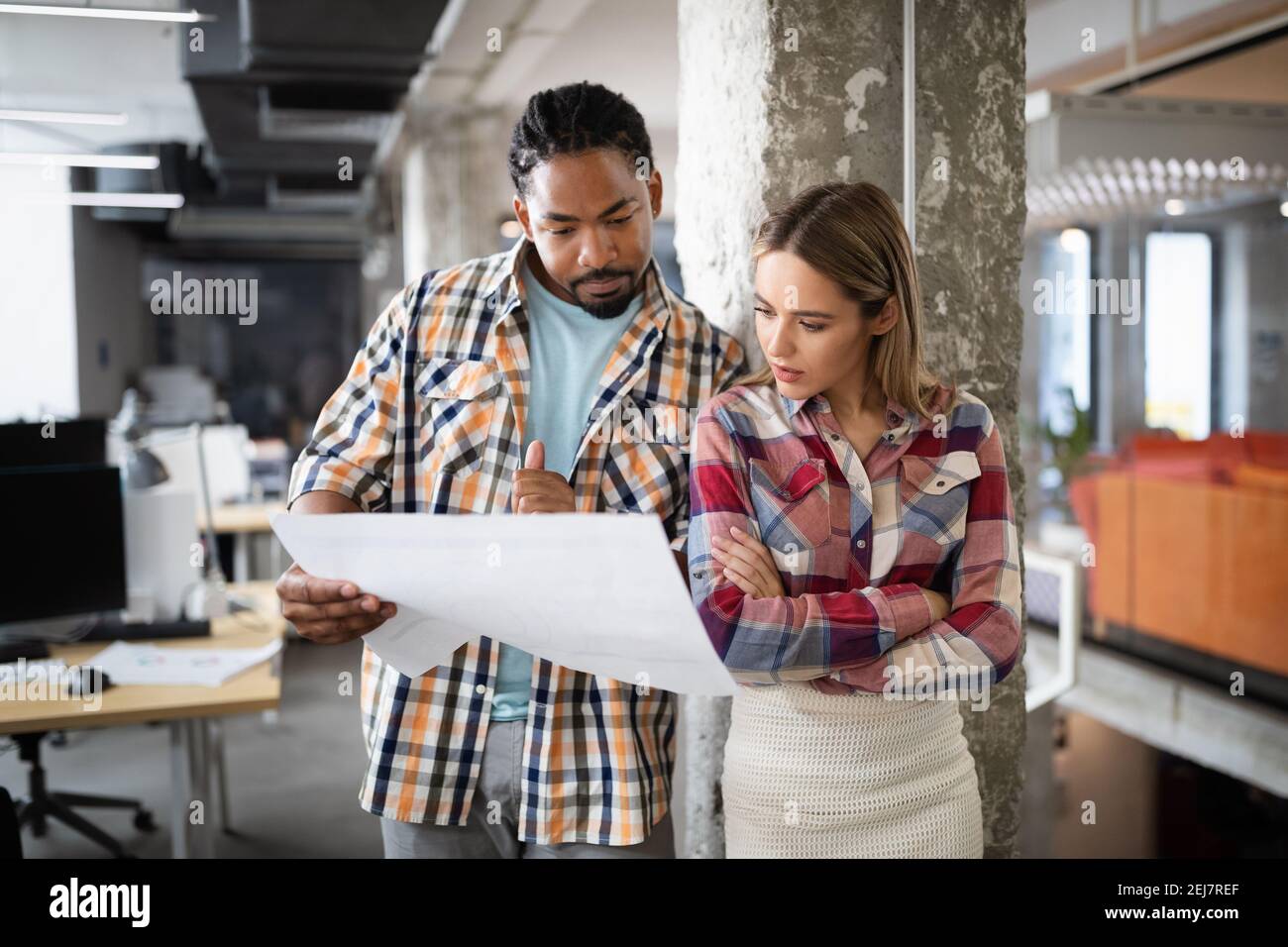Young architect colleagues are analyzing blueprints while working on a new project Stock Photo