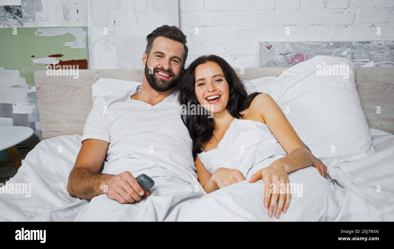 happy young couple smiling while watching movie in bedroom Stock Photo ...