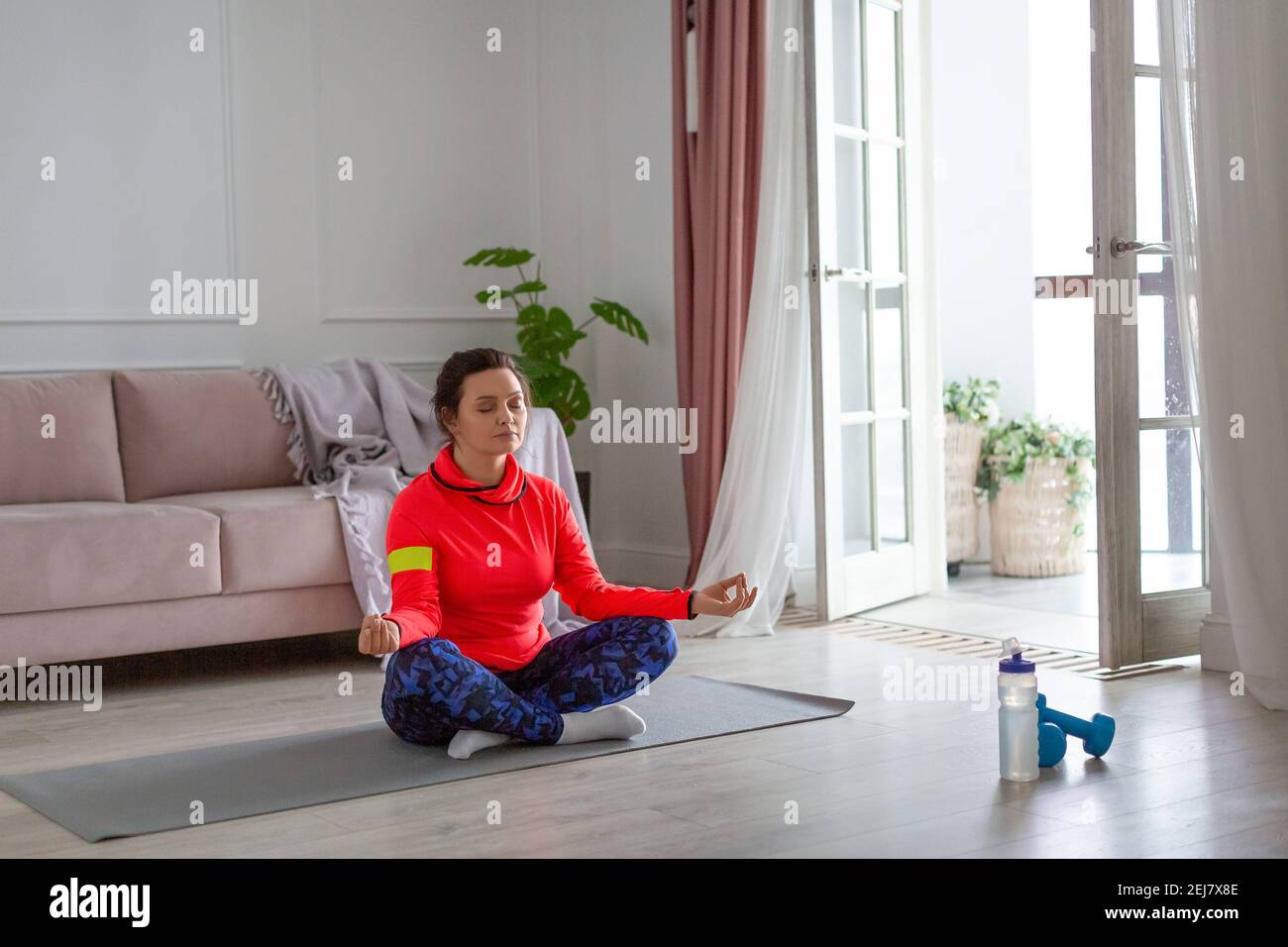 Woman doing yoga at home. She meditates sitting in the lotus position ...