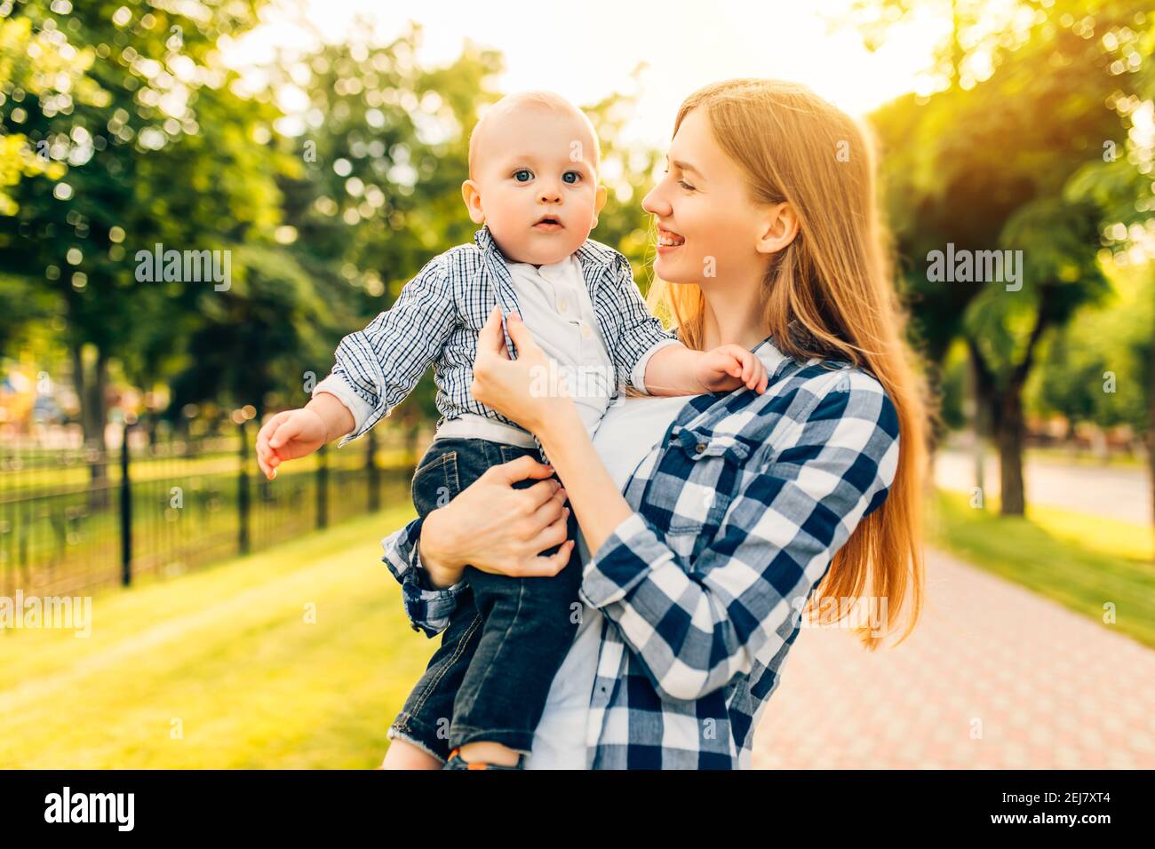 Happy beautiful young mom kissing and hugging her baby in the park on a