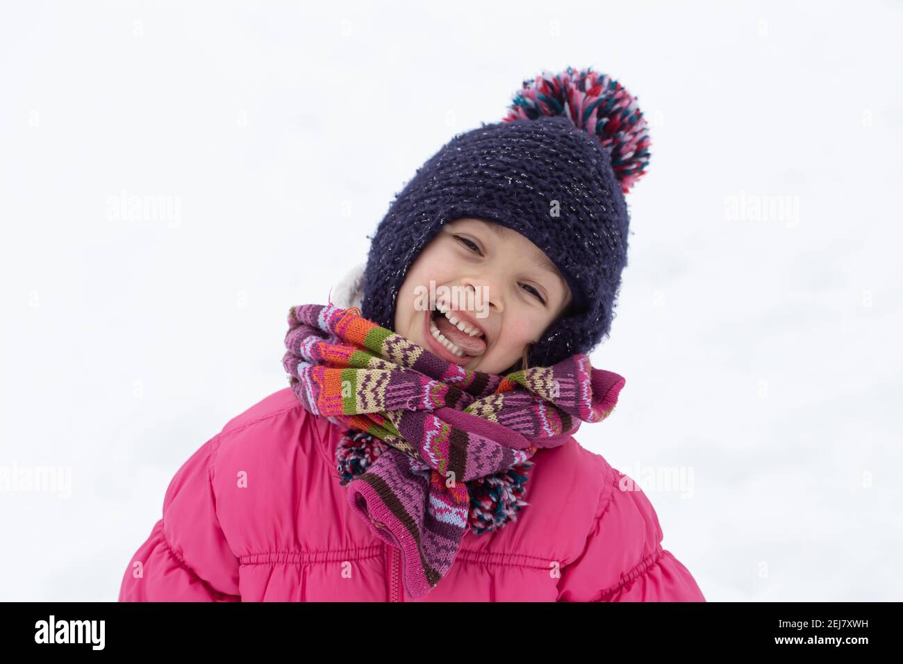 A cute little girl in a pink jacket and a hat is playing in the snow ...