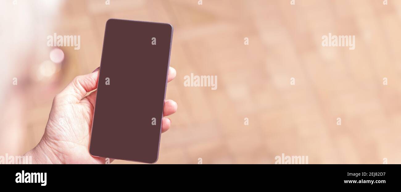 Elderly womans hand holding mobile cell phone. Over shoulder. Old woman looking at cell phone. Banner. Blanck mobile phone screen. Display media.  Stock Photo