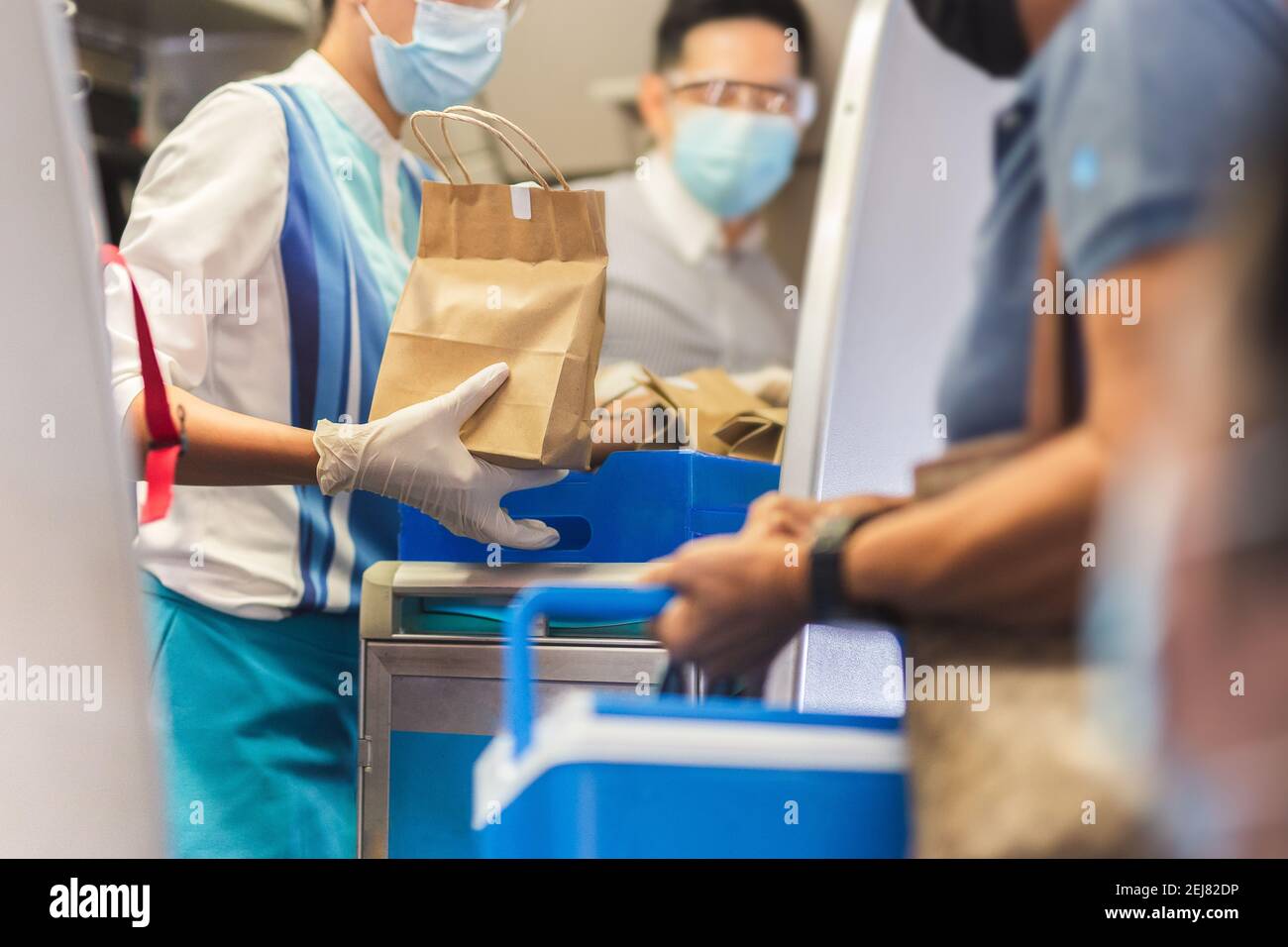Flight attendant in face mask with gloves giving meals to the passenger travel bubble. Stock Photo