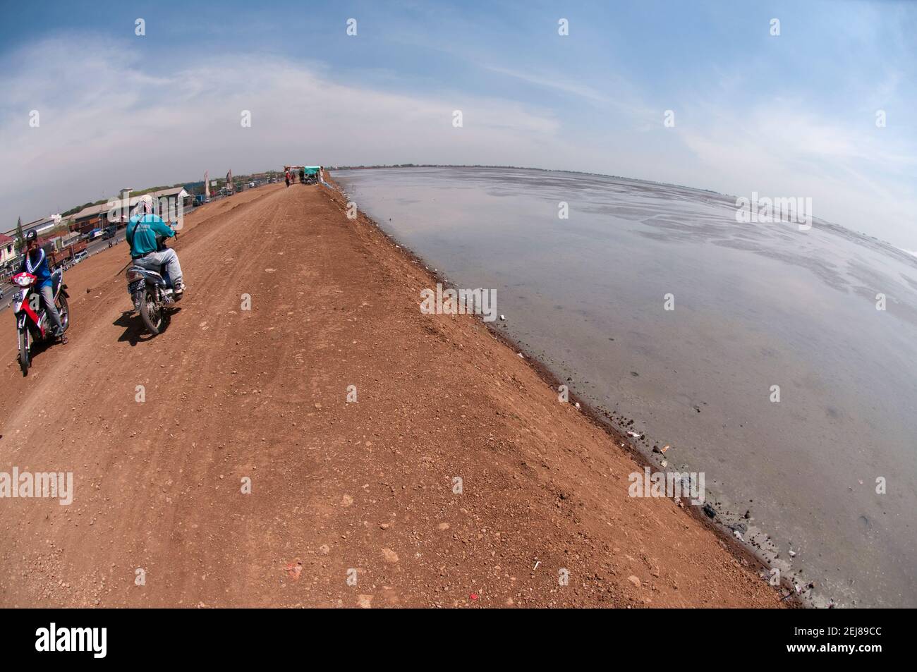 People riding motorbikes on levee surrounding mud lake environmental disaster which developed after drilling incident, Porong Sidoarjo, near Surabaya, Stock Photo