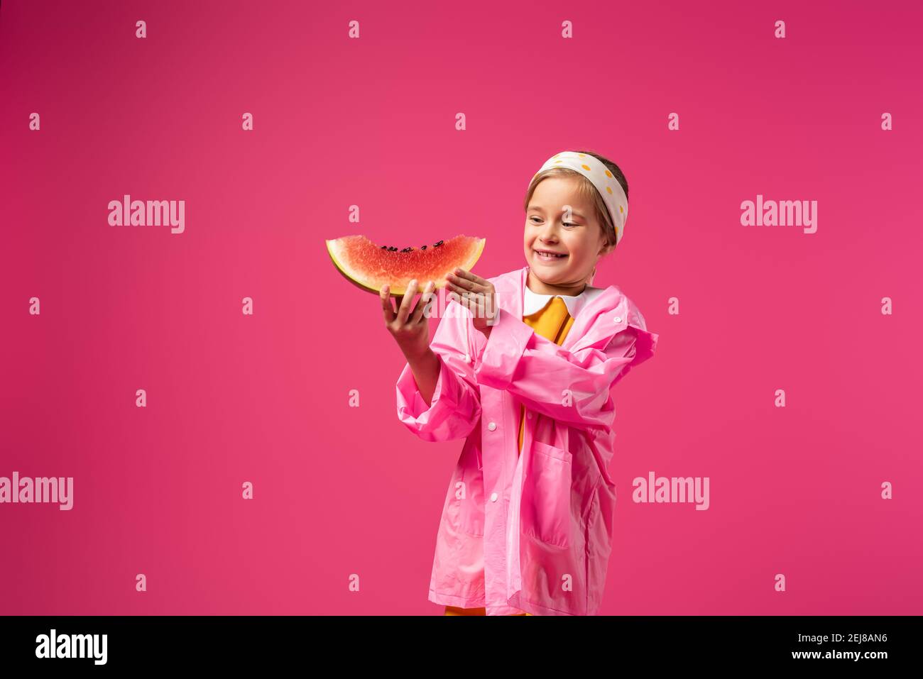 happy girl in raincoat holding watermelon on crimson Stock Photo