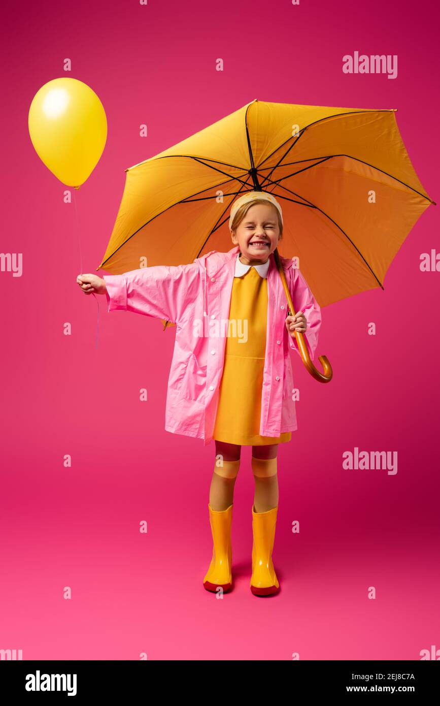 full length of excited girl in raincoat holding balloon and yellow umbrella  on crimson Stock Photo - Alamy