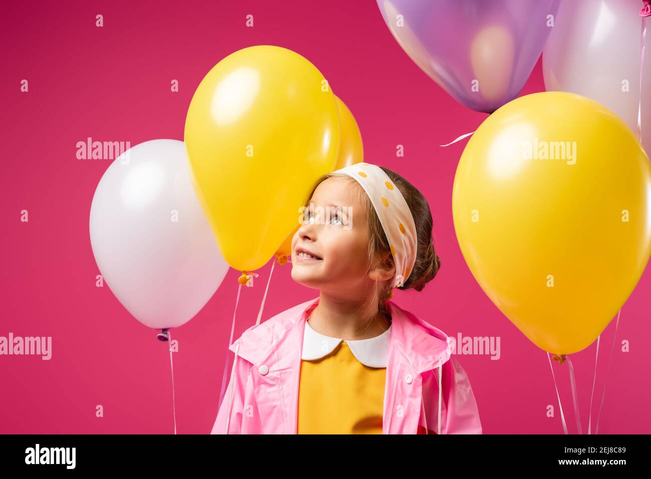 happy kid looking away near balloons isolated on crimson Stock Photo