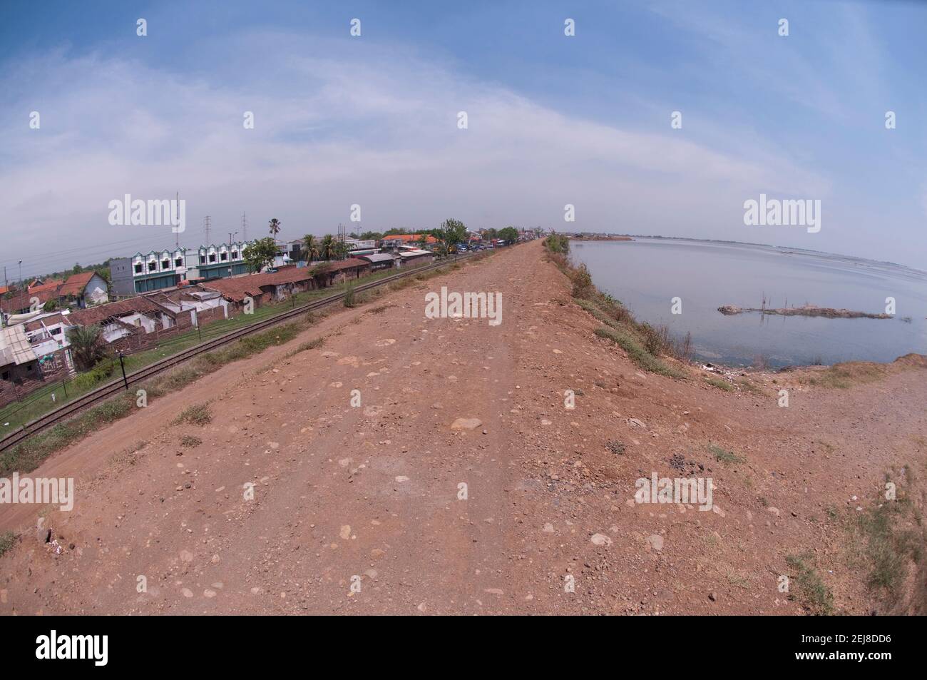 Levee seperating village with mud lake environmental disaster which developed after drilling incident, Porong Sidoarjo, near Surabaya, East Java, Indo Stock Photo