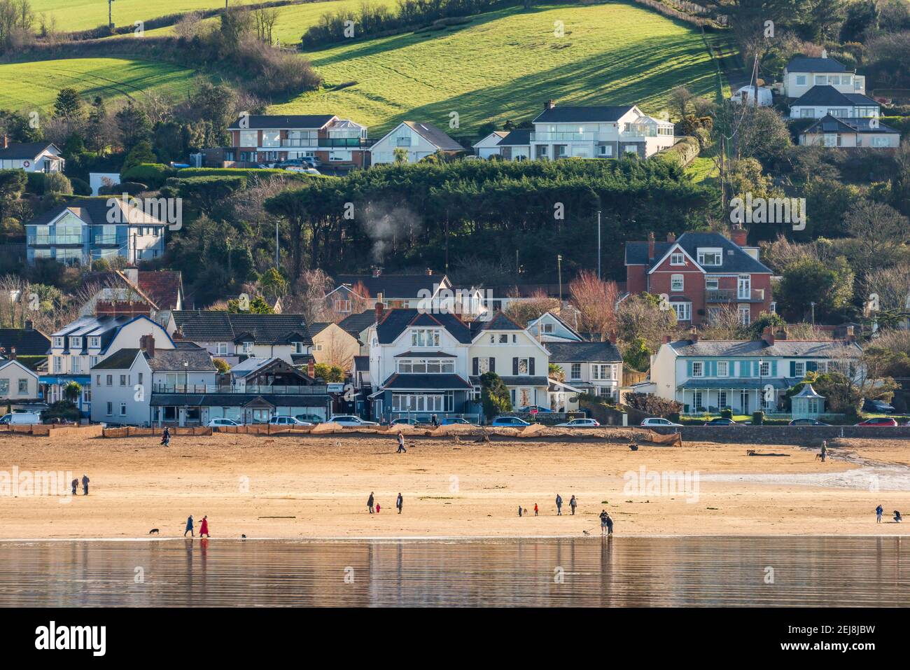 Instow, North Devon, England. Monday 22nd February 2021. UK Weather. After a week of grey skies in North Devon, a brighter start to the new week tempts people out for a 'socially distanced' walk on the beach for their daily exercise at the picturesque coastal village of Instow. Credit: Terry Mathews/Alamy Live News Stock Photo
