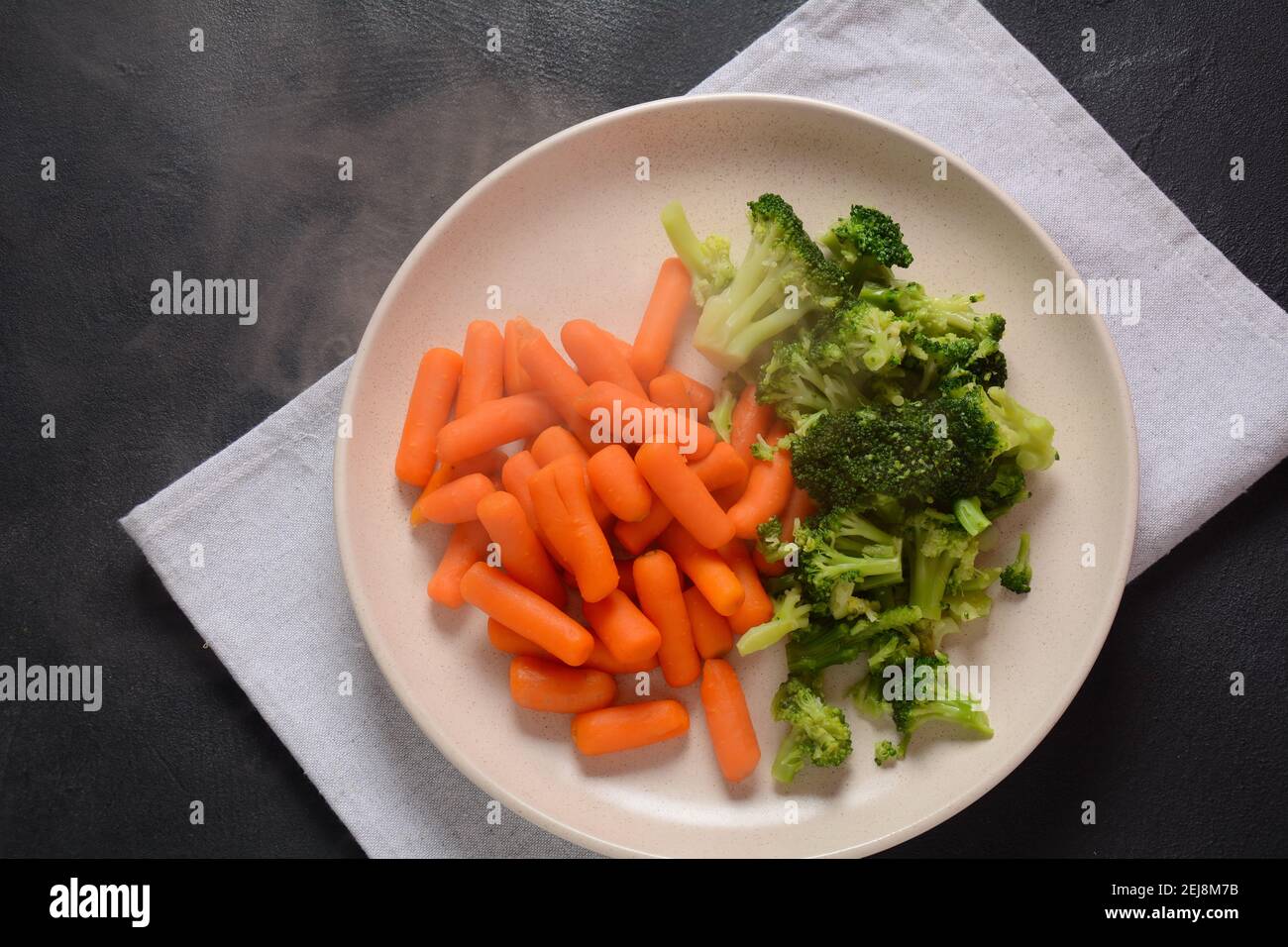Bunch of cooked small boiled carrots and broccoli on white plate