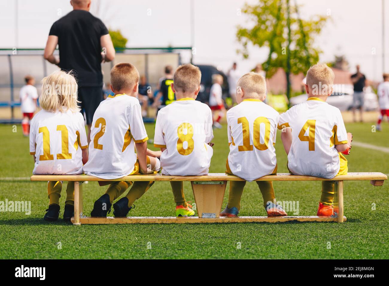 Group of Children in Soccer Jerseys with Golden Player Numbers. Football Team on Bench. Group of Young Boys with School Sports Coach Trainer. Youth Fo Stock Photo