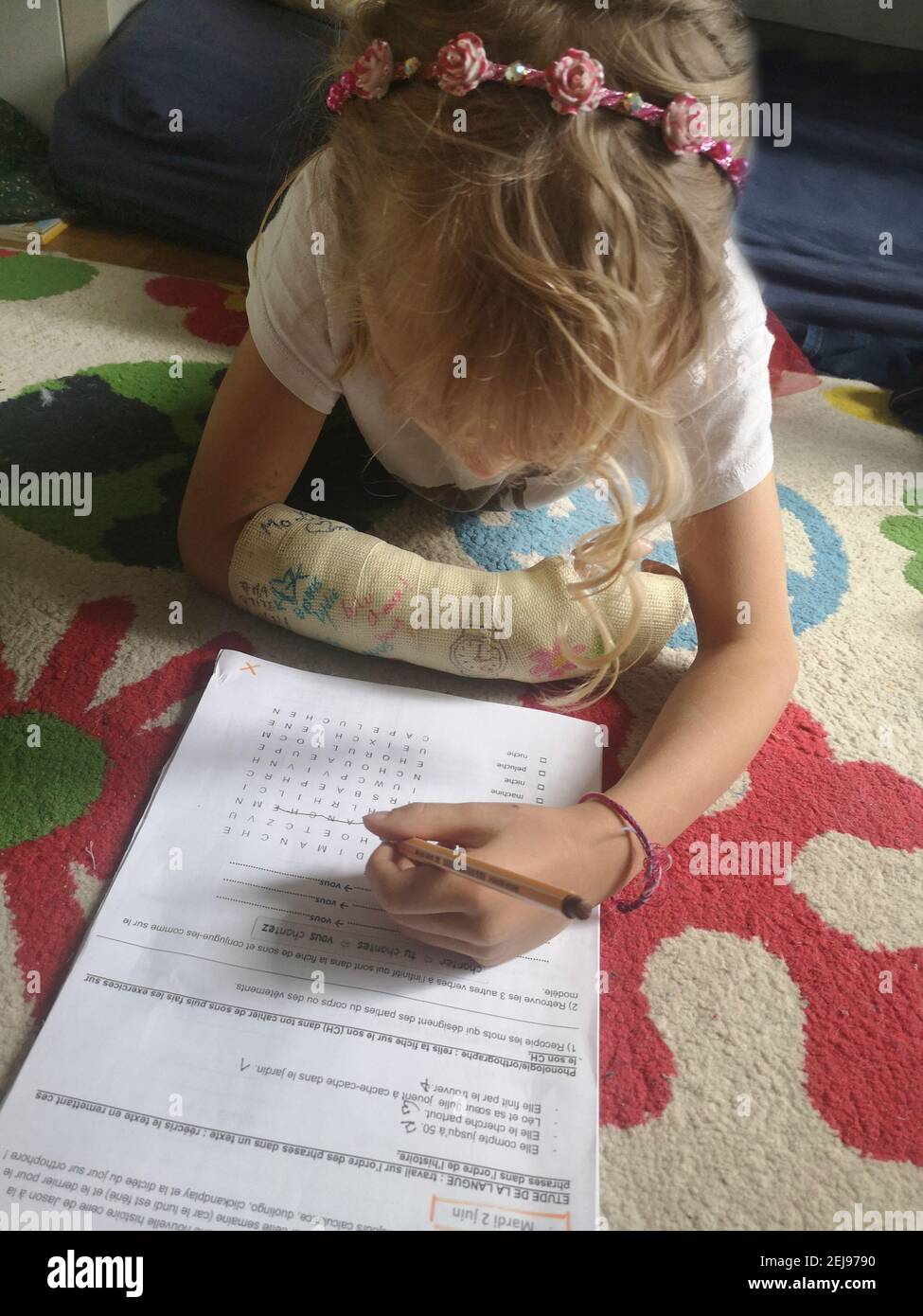 7-9 year old European girl with a plastered broken arm doing her homework with her left hand, France. Stock Photo