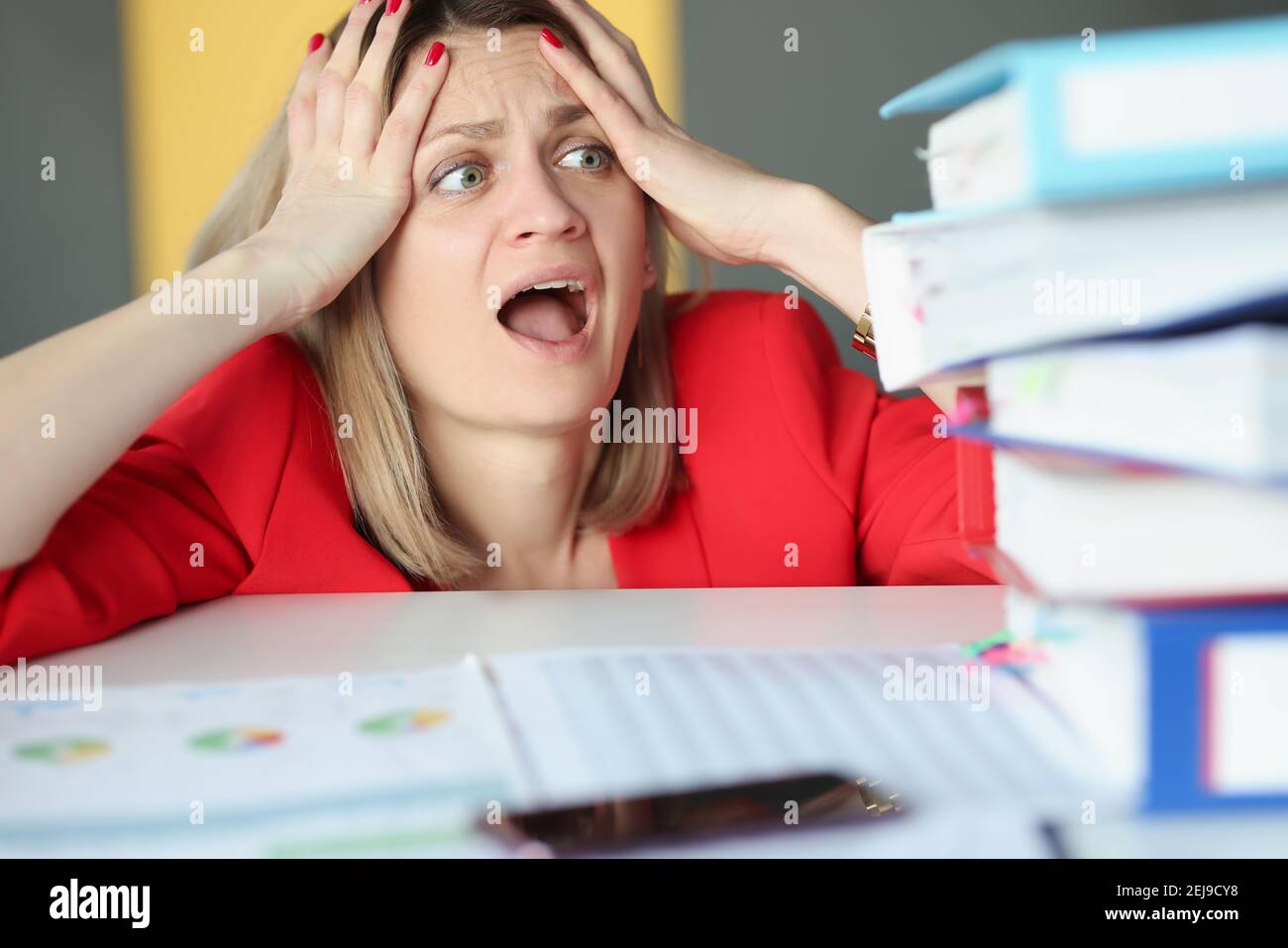 Woman holding her head and is surprised in front of many folders on table Stock Photo