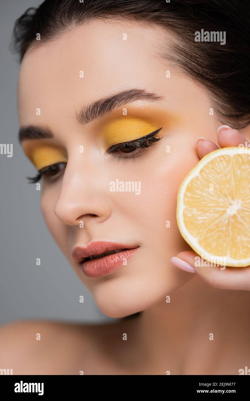 close up of young woman holding half of ripe lemon isolated on grey Stock Photo