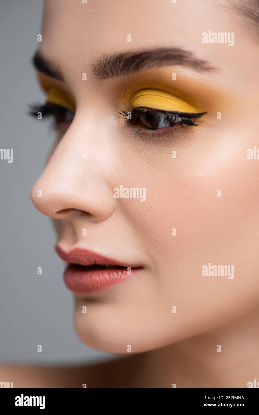 close up of young woman with yellow eyeshadow looking away isolated on grey Stock Photo