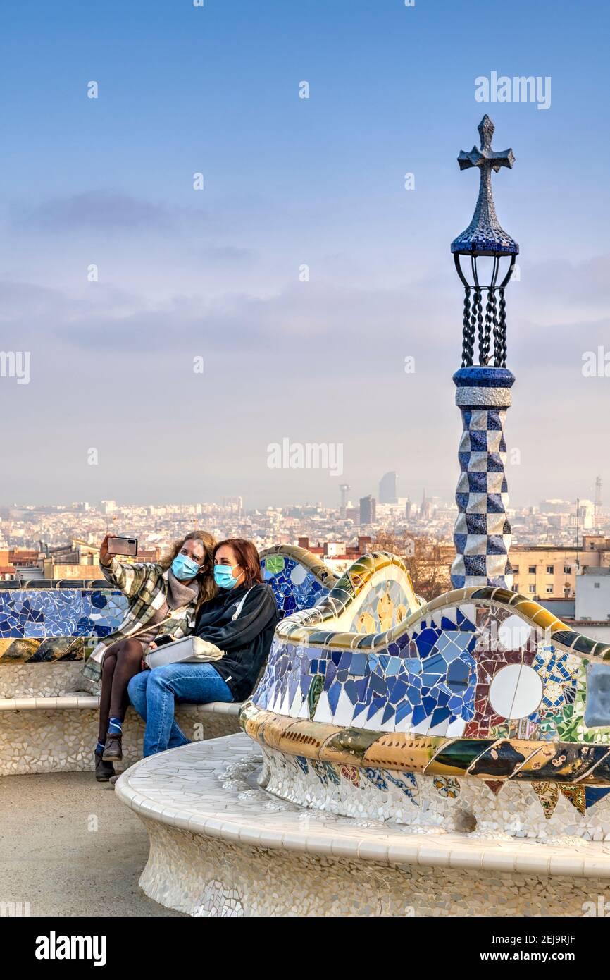 Two women wearing surgical masks talking selfie with smartphone at sunset at Park Guell, Barcelona, Catalonia, Spain Stock Photo