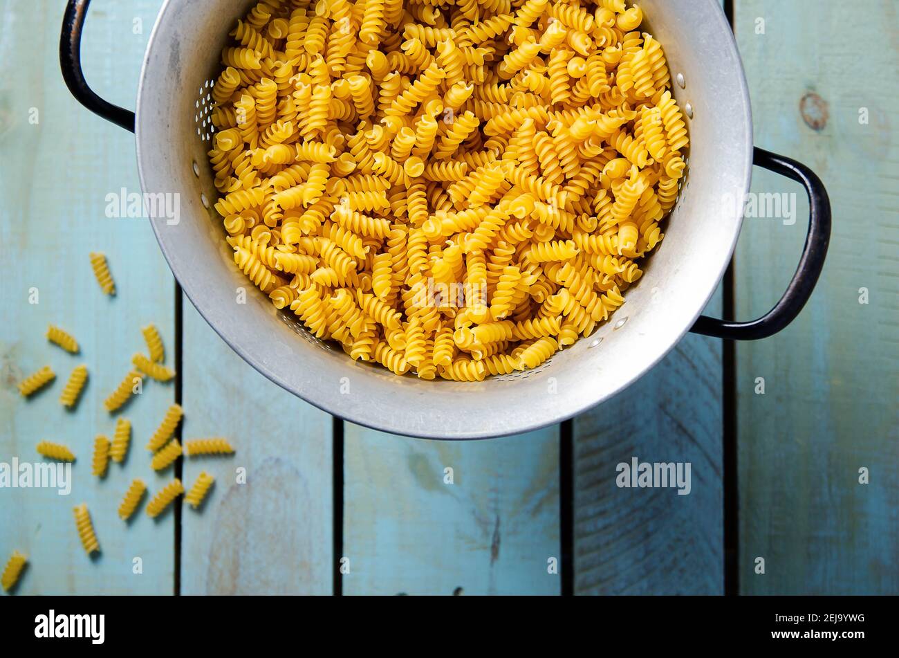 Uncooked spiral pasta in a strainer in a light blue backdrop. Top view. Stock Photo