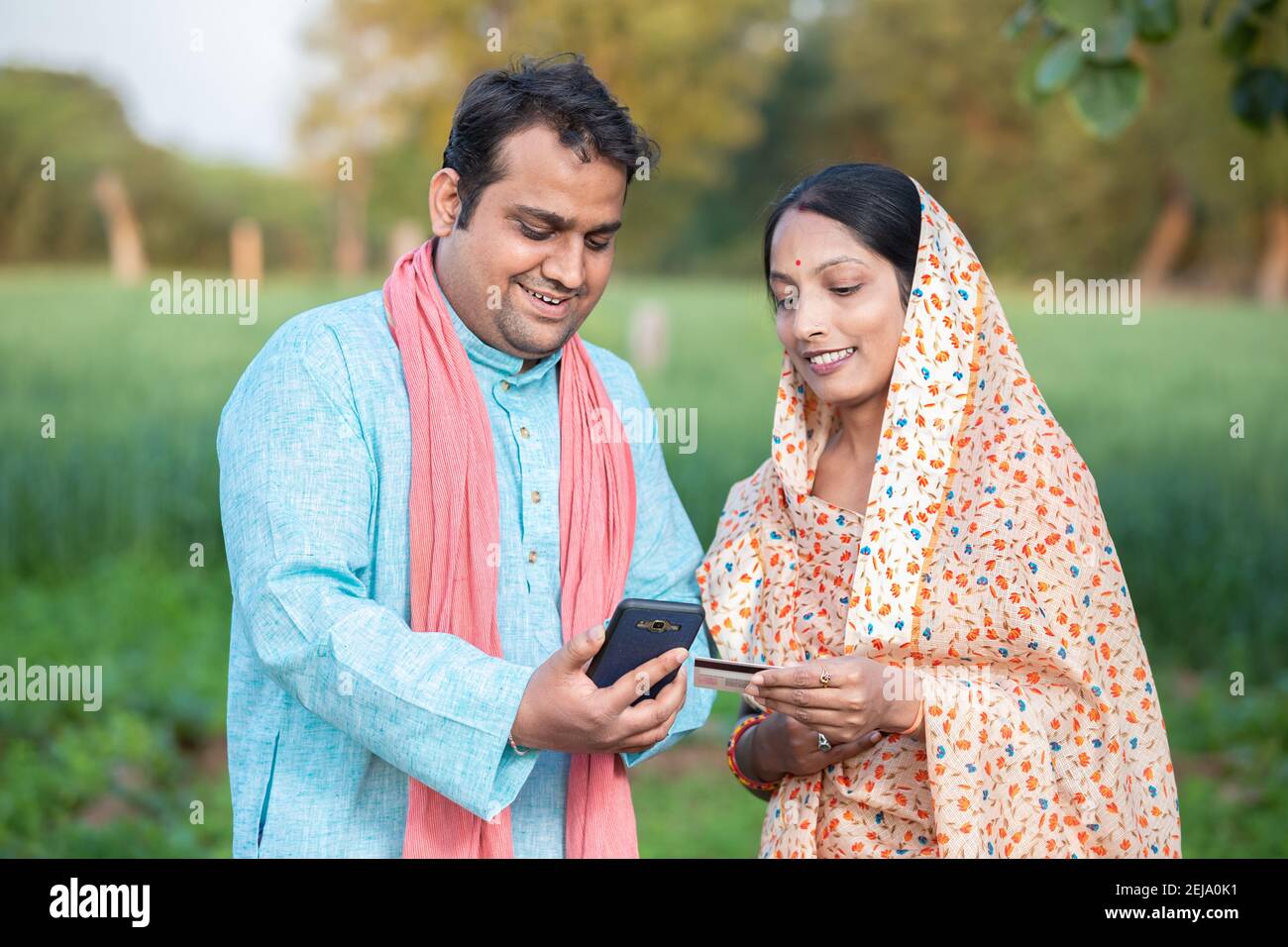Happy indian rural farmer couple using smartphone to make online payment with debit card in agricultural field, shopping on internet with cellphone se Stock Photo