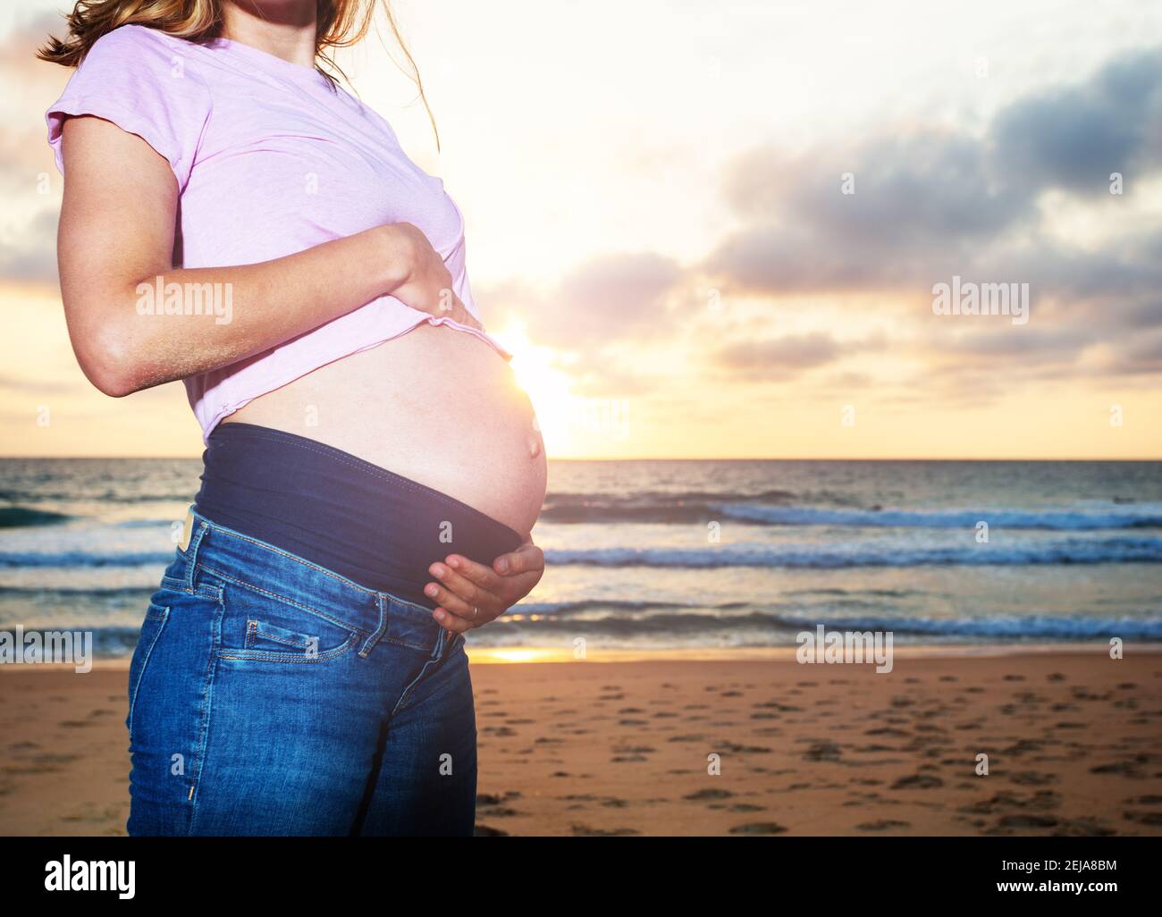 Close Photo Of A Pregnant Woman During Vacations On The Sand Beach Touch Belly Over Sunset Stock