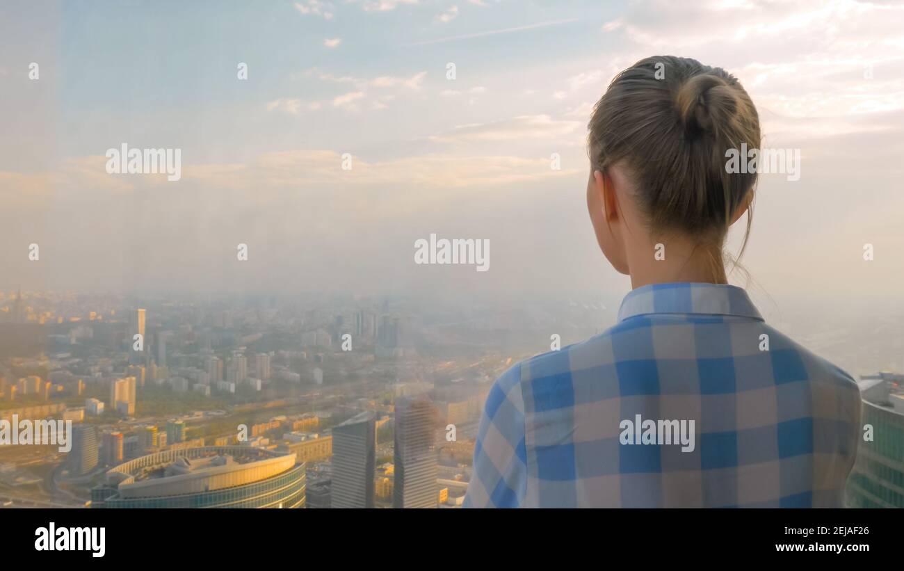 Back view of woman looking at spectacular cityscape through window of ...