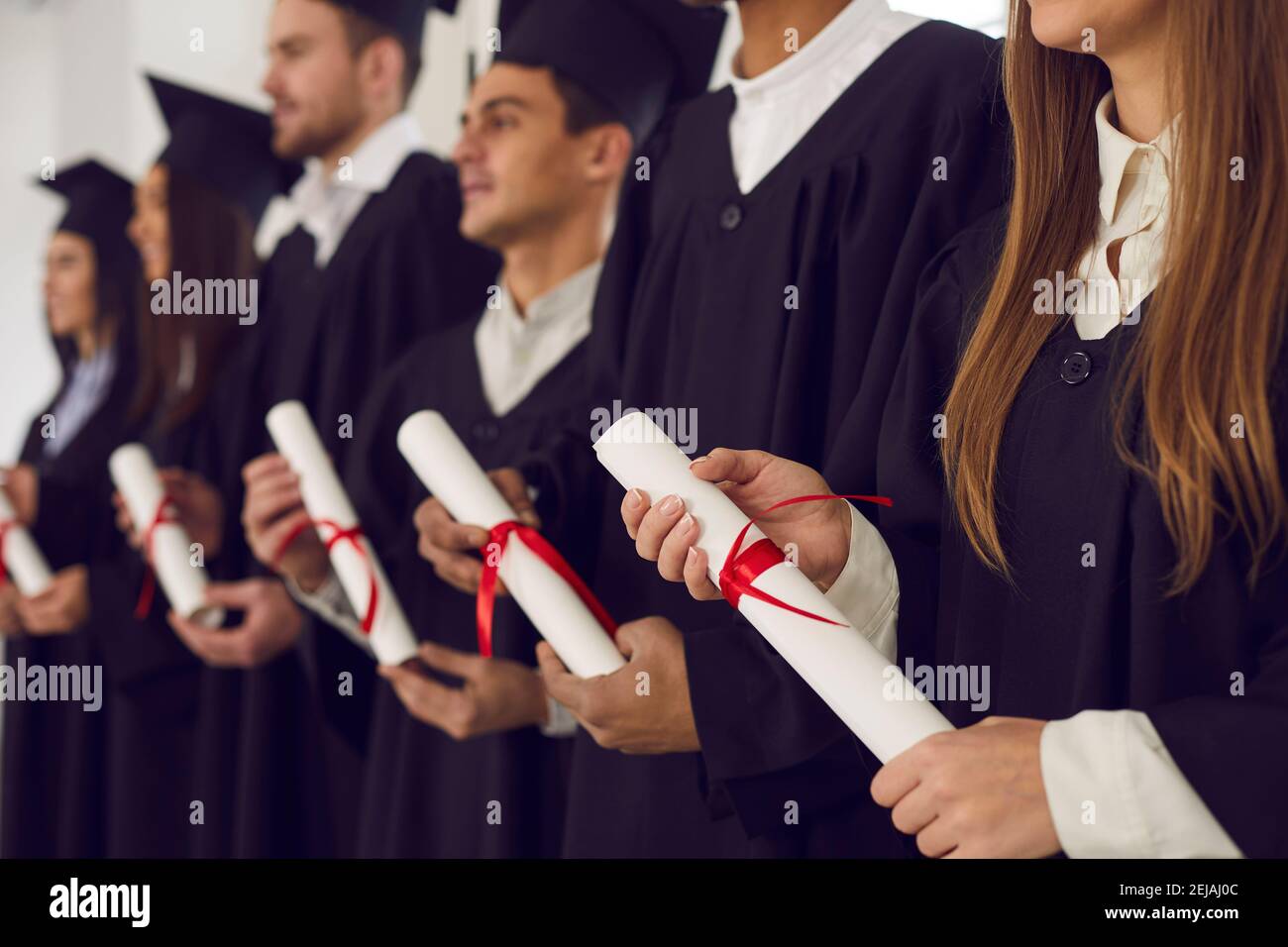 Row of graduates in black caps and gowns holding diplomas at graduation ceremony Stock Photo