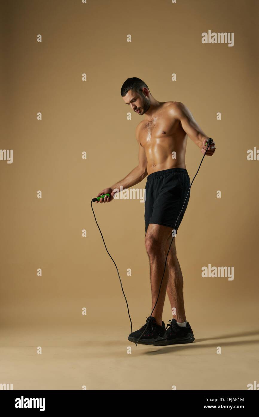 Portrait of adorable Caucasian sportsman in black sportswear holding skip rope in hands while standing in the studio isolated on yellow background Stock Photo