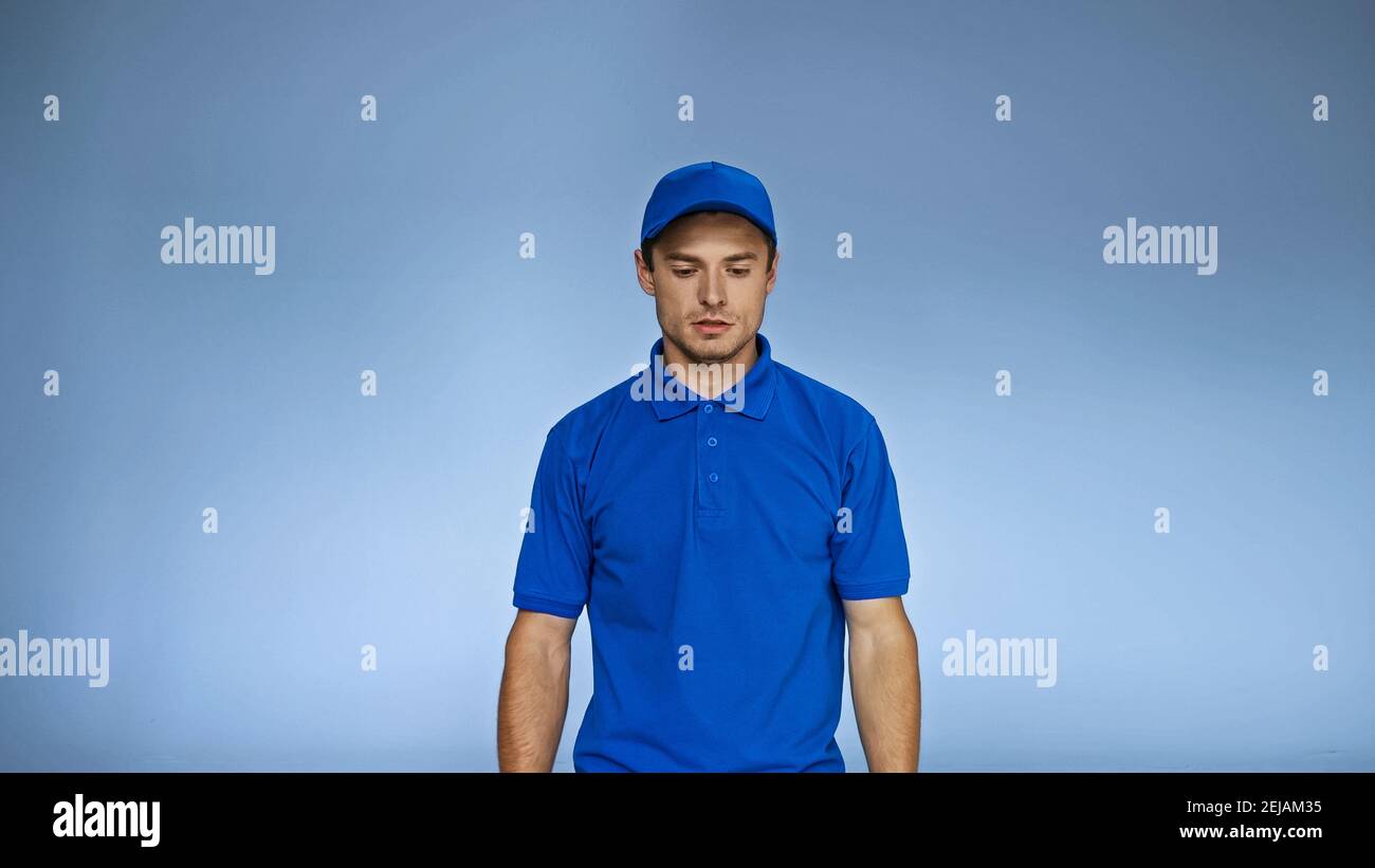 upset delivery man in uniform standing isolated on blue Stock Photo