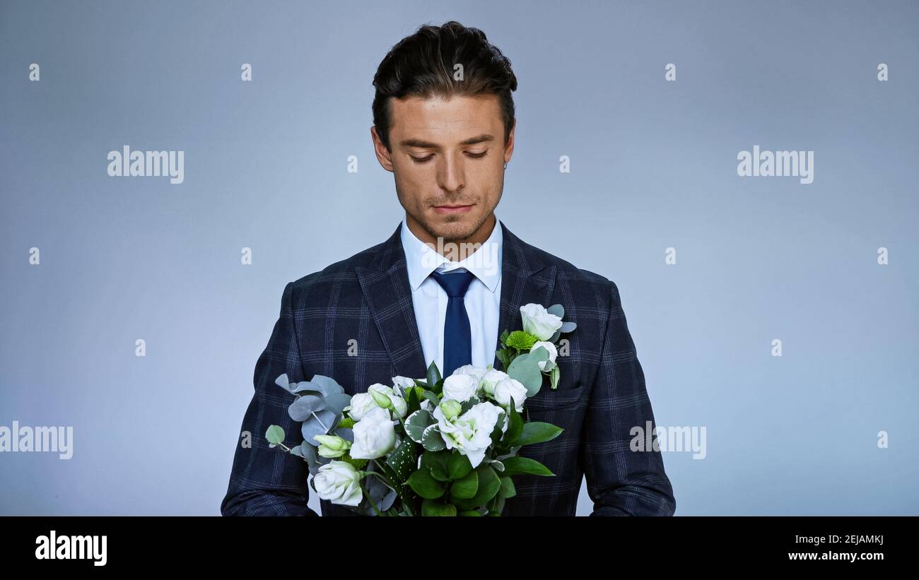 upset bridegroom holding wedding bouquet isolated on blue Stock Photo