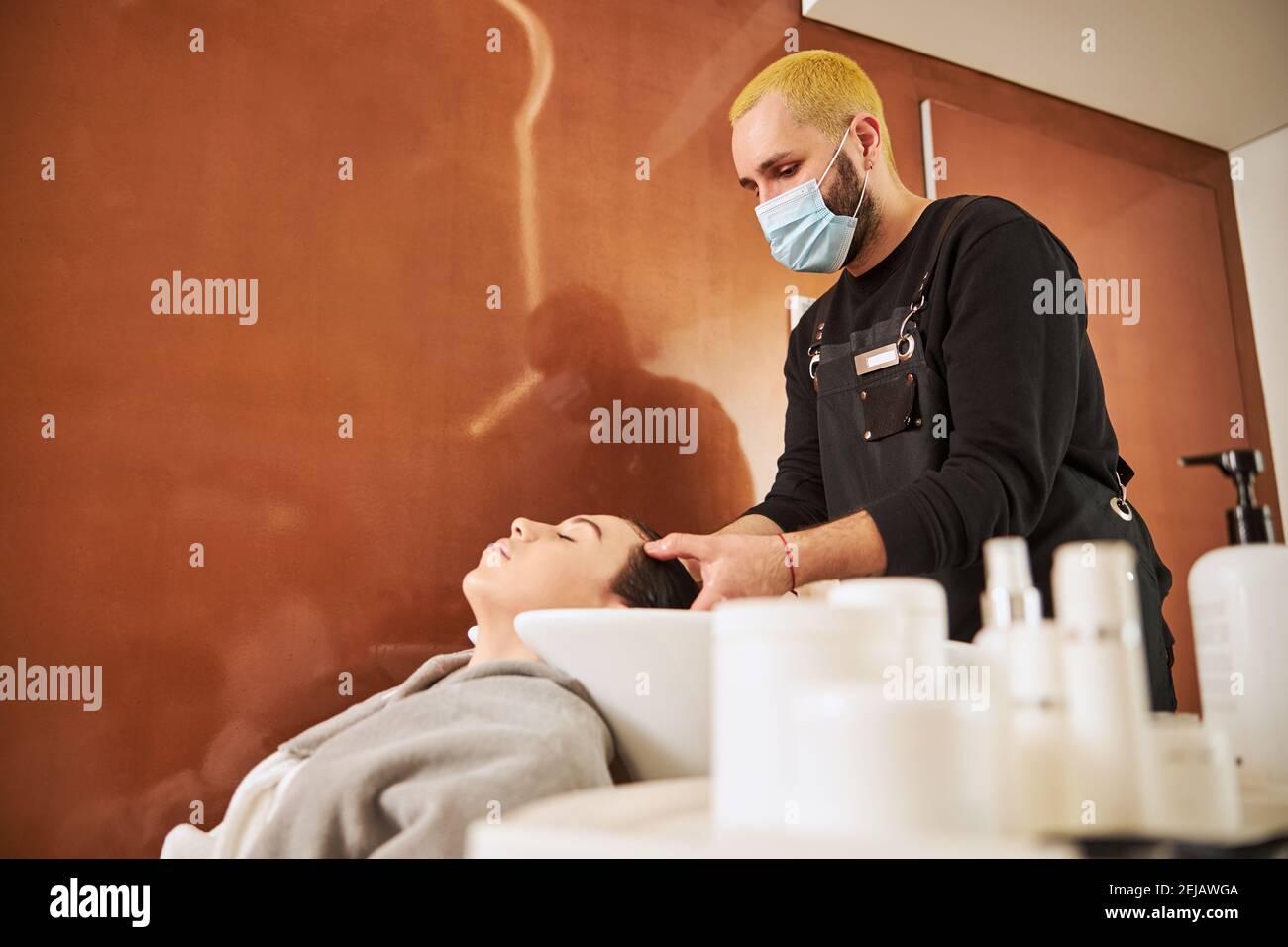 Hairdresser evenly distributing the styling product over the client scalp Stock Photo