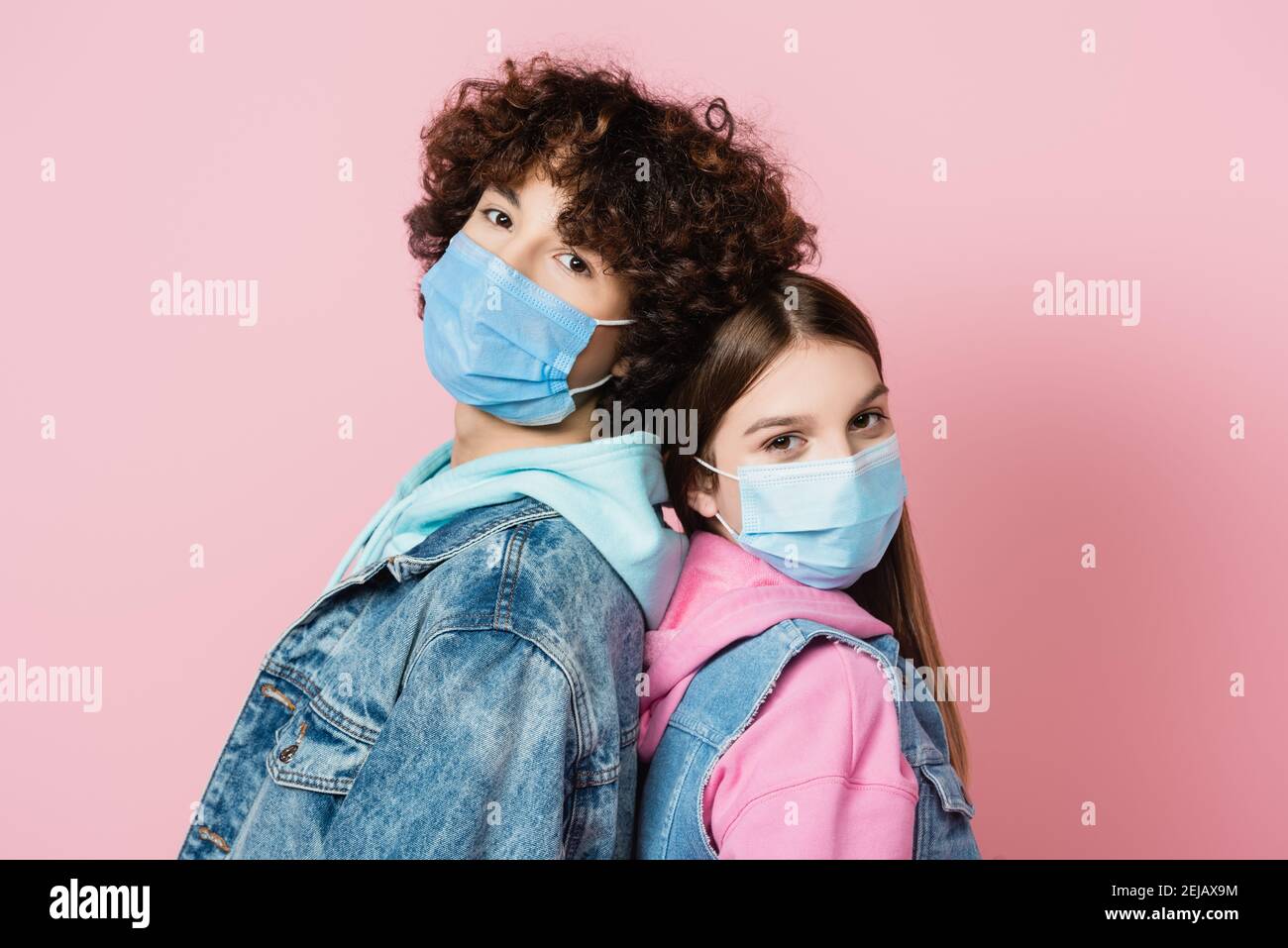 Teenagers in protective masks looking at camera while standing back to ...