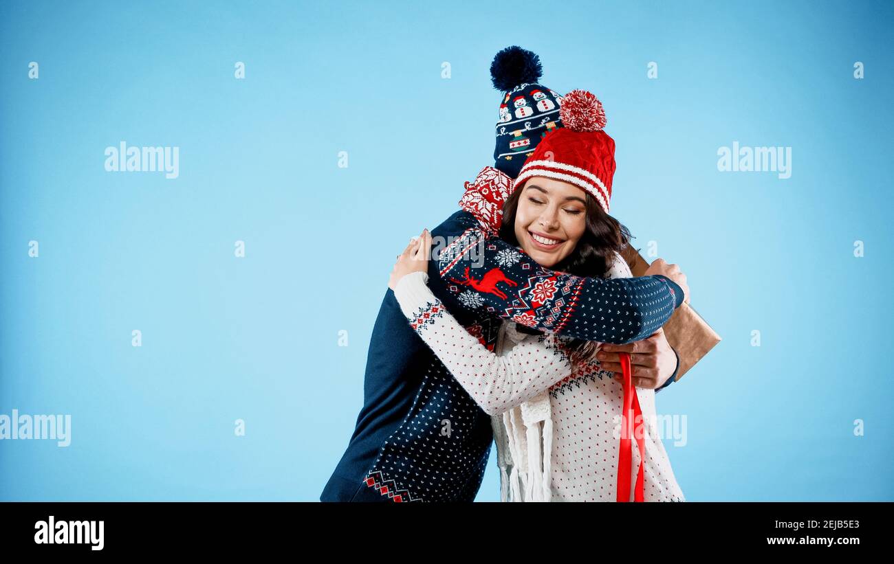 Hugging Sweater Smiling woman in hat and sweater hugging boyfriend with gift box on ...