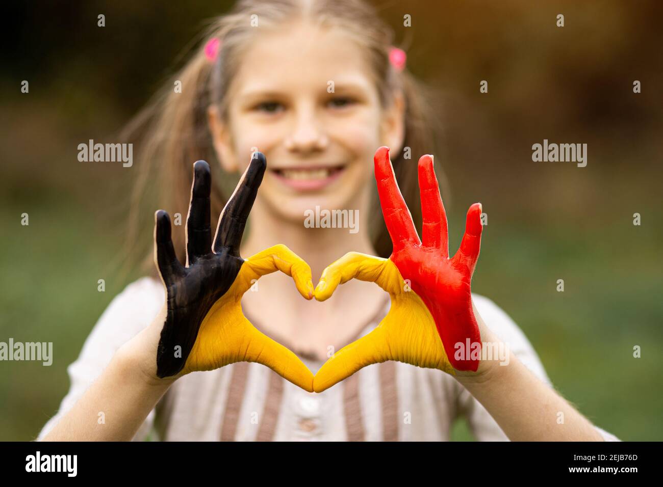 Kid hands painted in Belgium flag color show symbol of heart and love gesture on nature background. Focus on hands Stock Photo