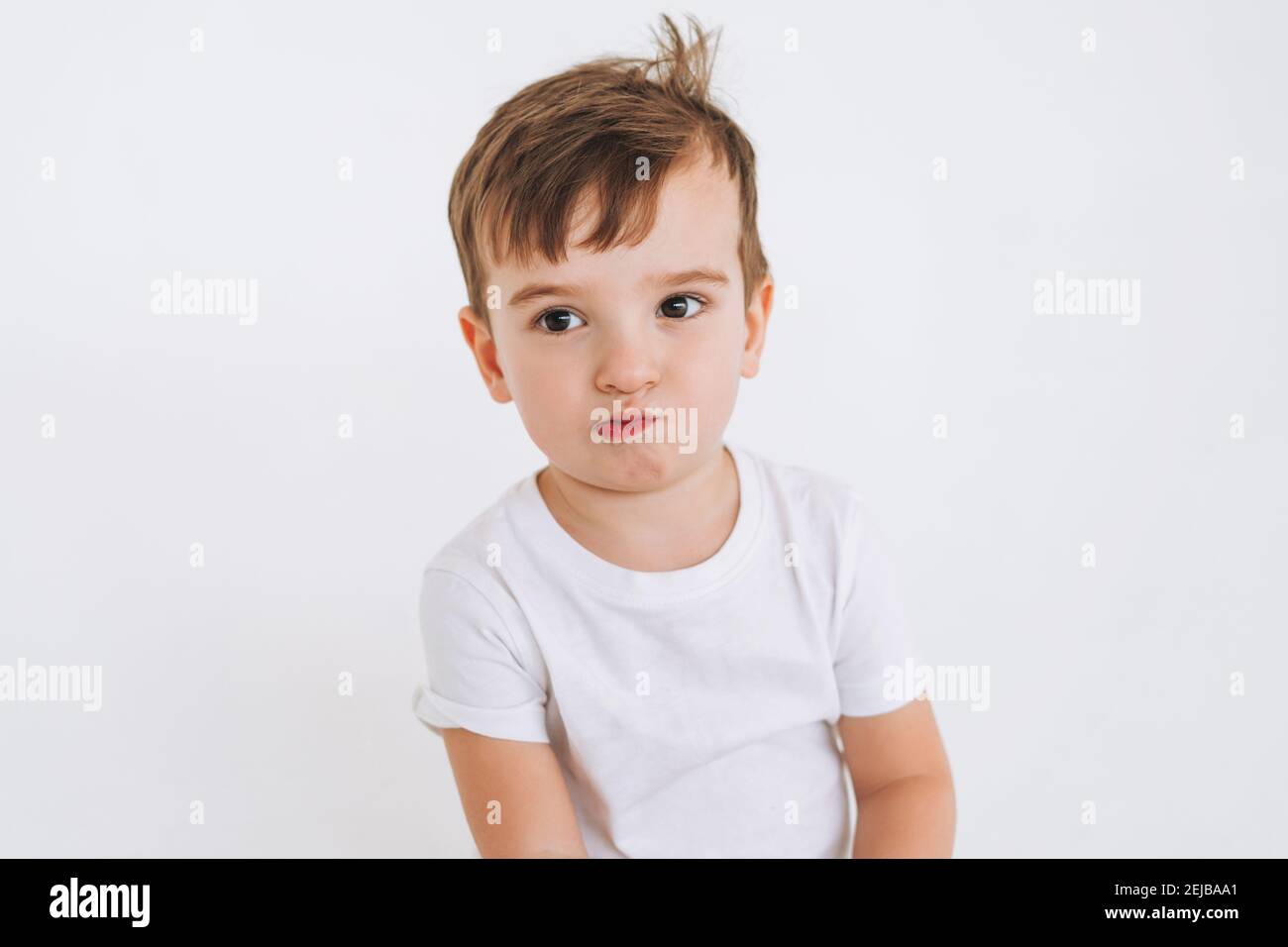 Funny cute thoughtful toddler boy in white t-shirt on white background Stock Photo