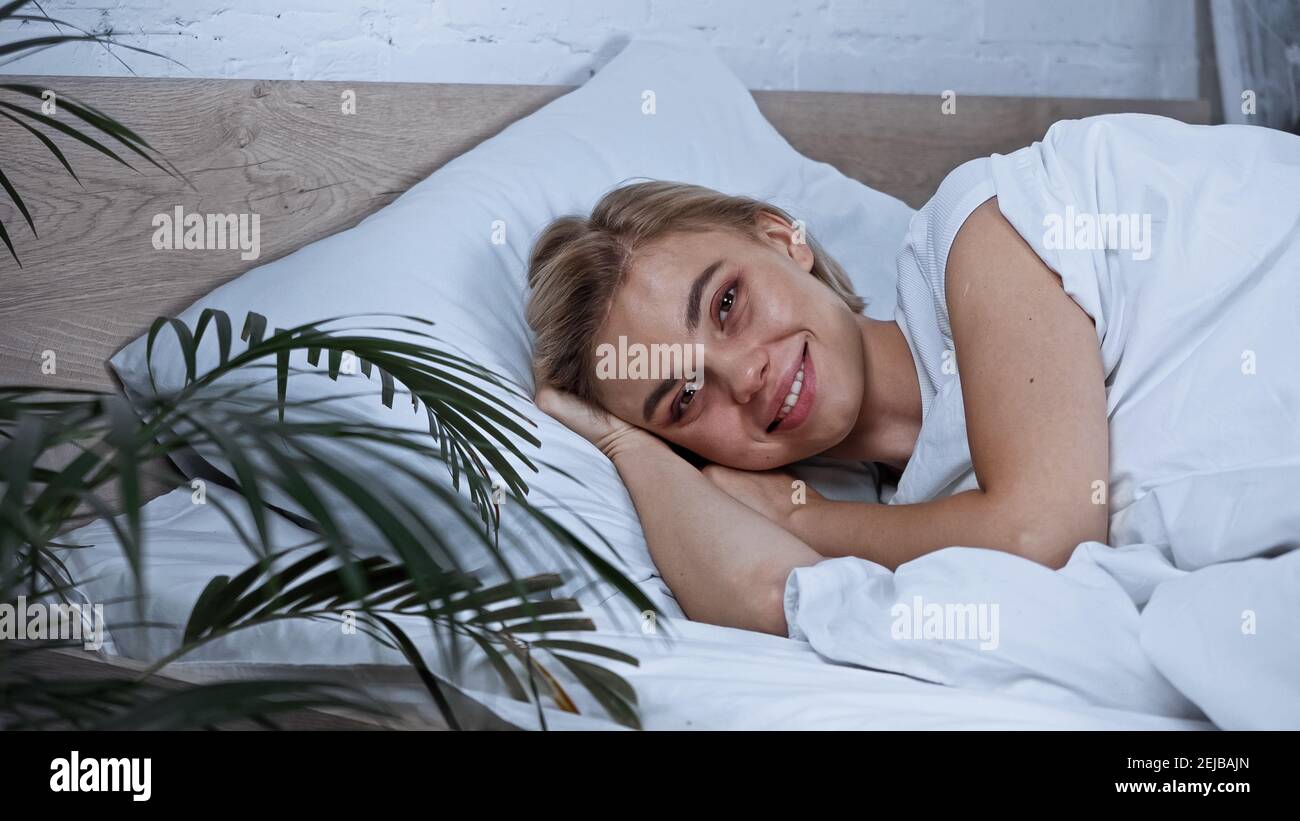 young joyful woman looking at camera while lying in bed on blurred foreground Stock Photo