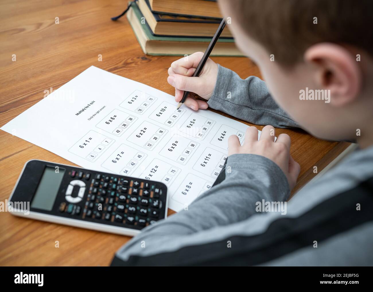 Young boy doing maths homework test times tables multiplication exam sat at table homeschooling calculator and books and pencil learning mathematics Stock Photo