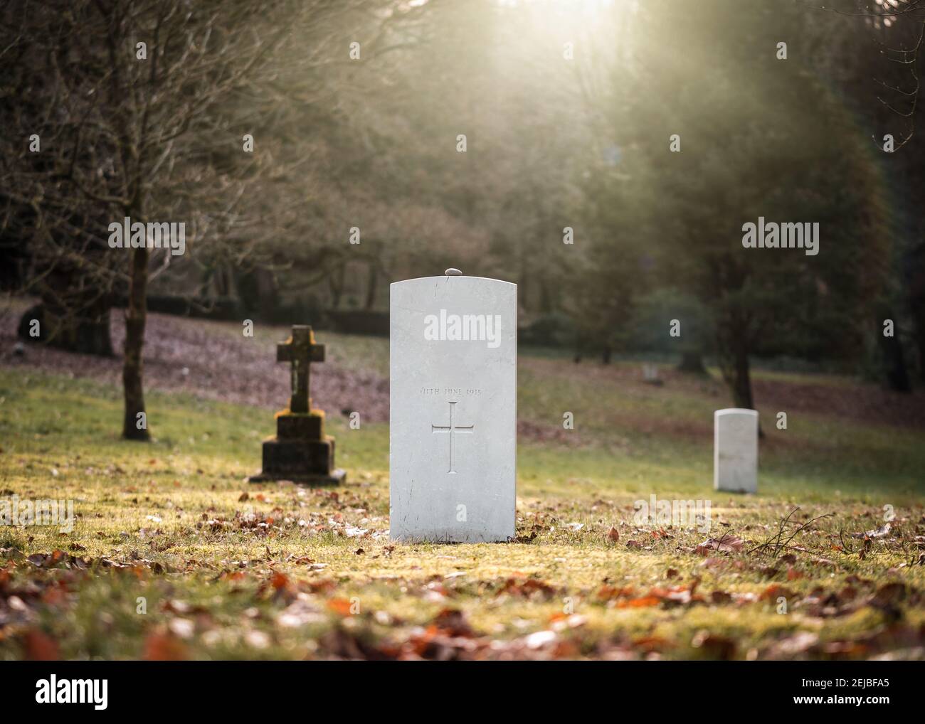 Military white British war grave with no inscription unknown soldier alone with sun rays shining peaceful tranquil down through trees WW1 World War 2 Stock Photo