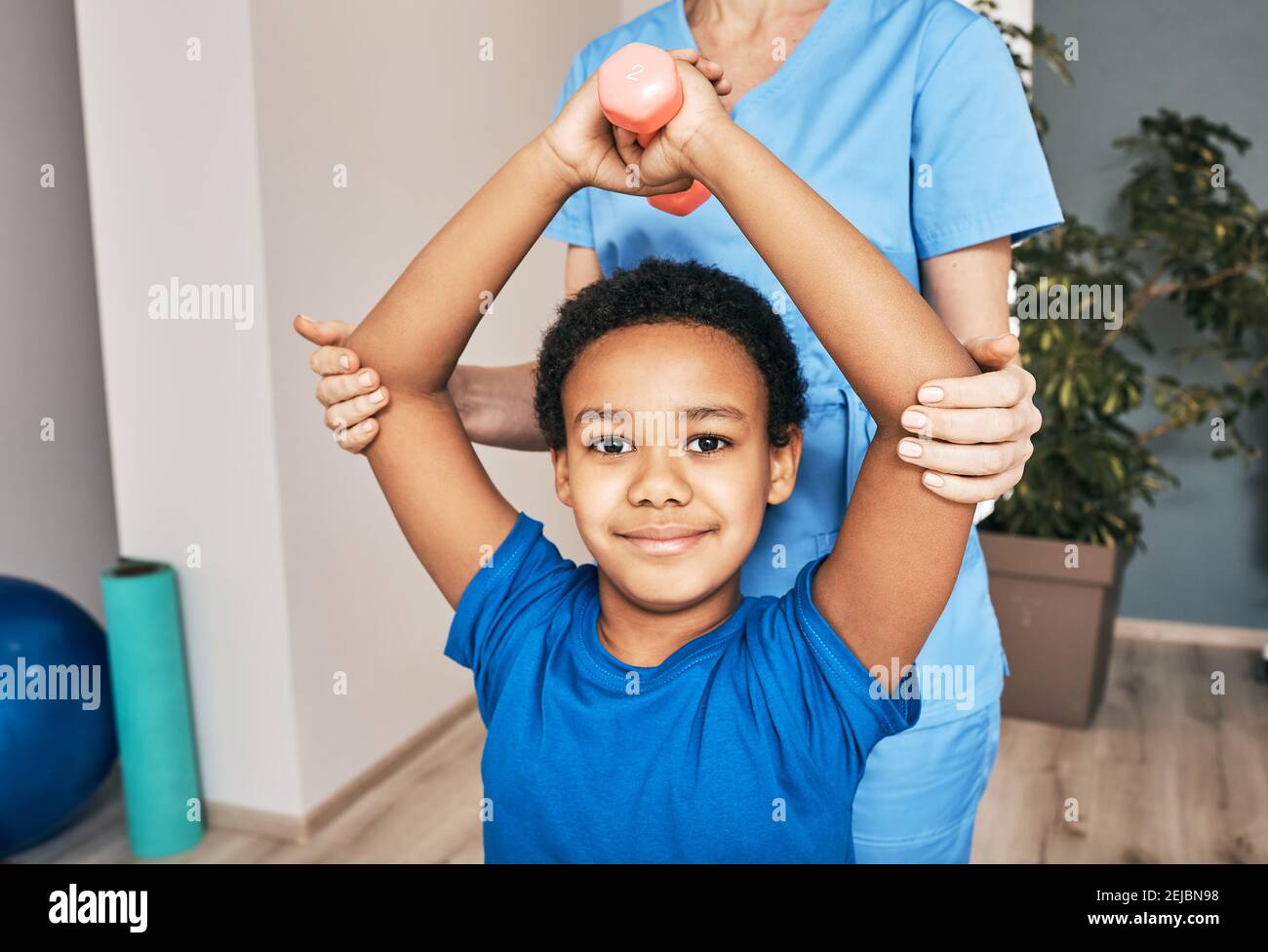African American boy lifts dumbbells, physical therapist helps exercise