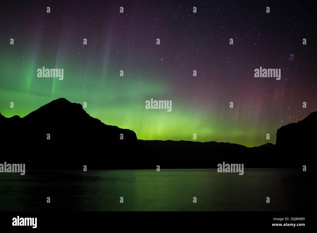Red, Green and yellow Aurora Borealis (Northern Lights) from a lake in the Canadian Rockies during a spring night, Lake Minnewanka, Banff, Canada Stock Photo