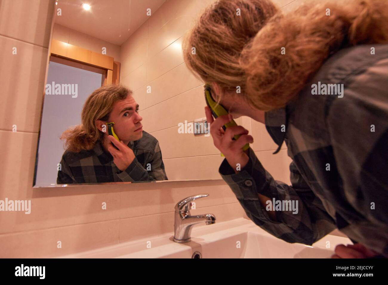 Handsome Caucasian man shaving his beard with a trimmer in a bathroom