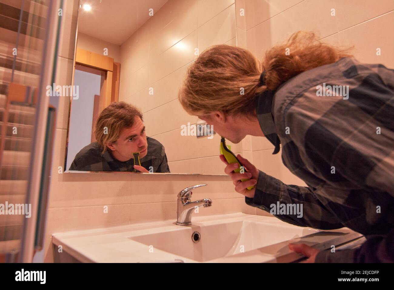 Handsome Caucasian man shaving his beard with a trimmer in a bathroom