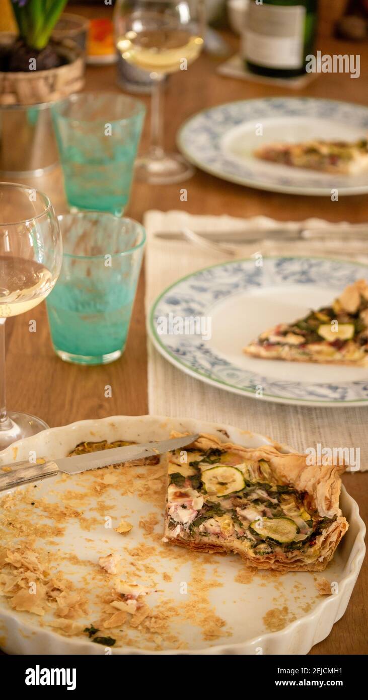 Festive lunch with friends, homemade vegetarian quiche with zucchini, Swiss chard and cheese, white wine. Turquoise water glasses. Stock Photo