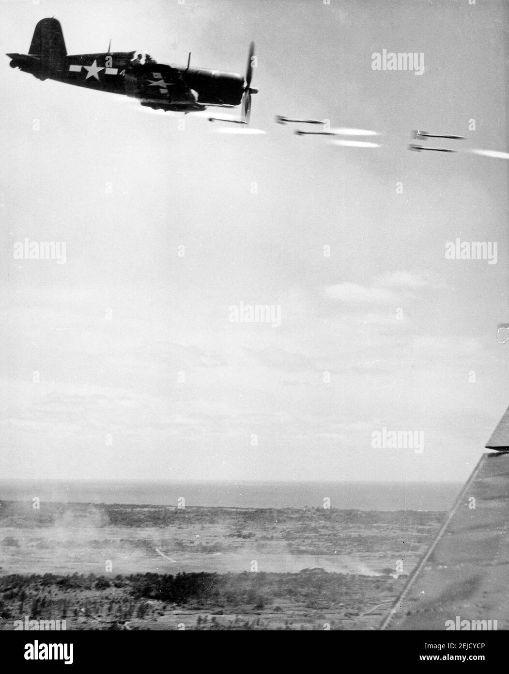 Corsair fighter looses its load of rocket projectiles on a run against a Japanese stronghold on Okinawa. In the lower background is the smoke of battle as Marine units move in to follow up with a Sunday punch, June 1945 Stock Photo