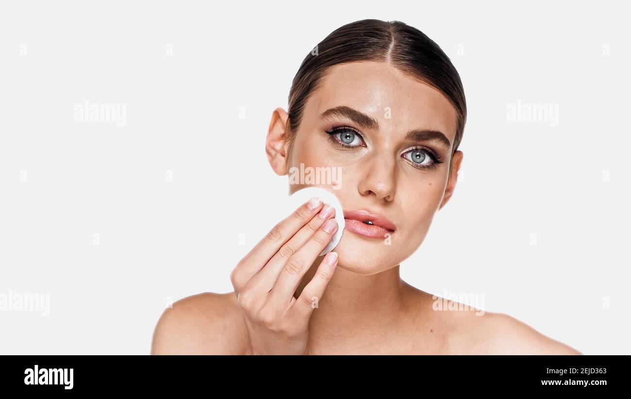 Young woman removing makeup with cotton pad isolated on white Stock