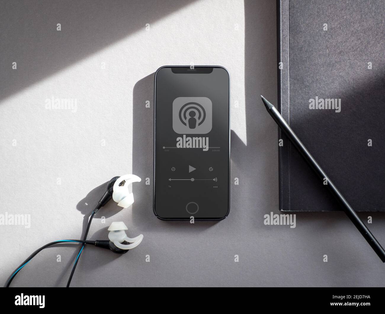 Black phone with a podcast playing and a notebook and earphones next to it. Stock Photo