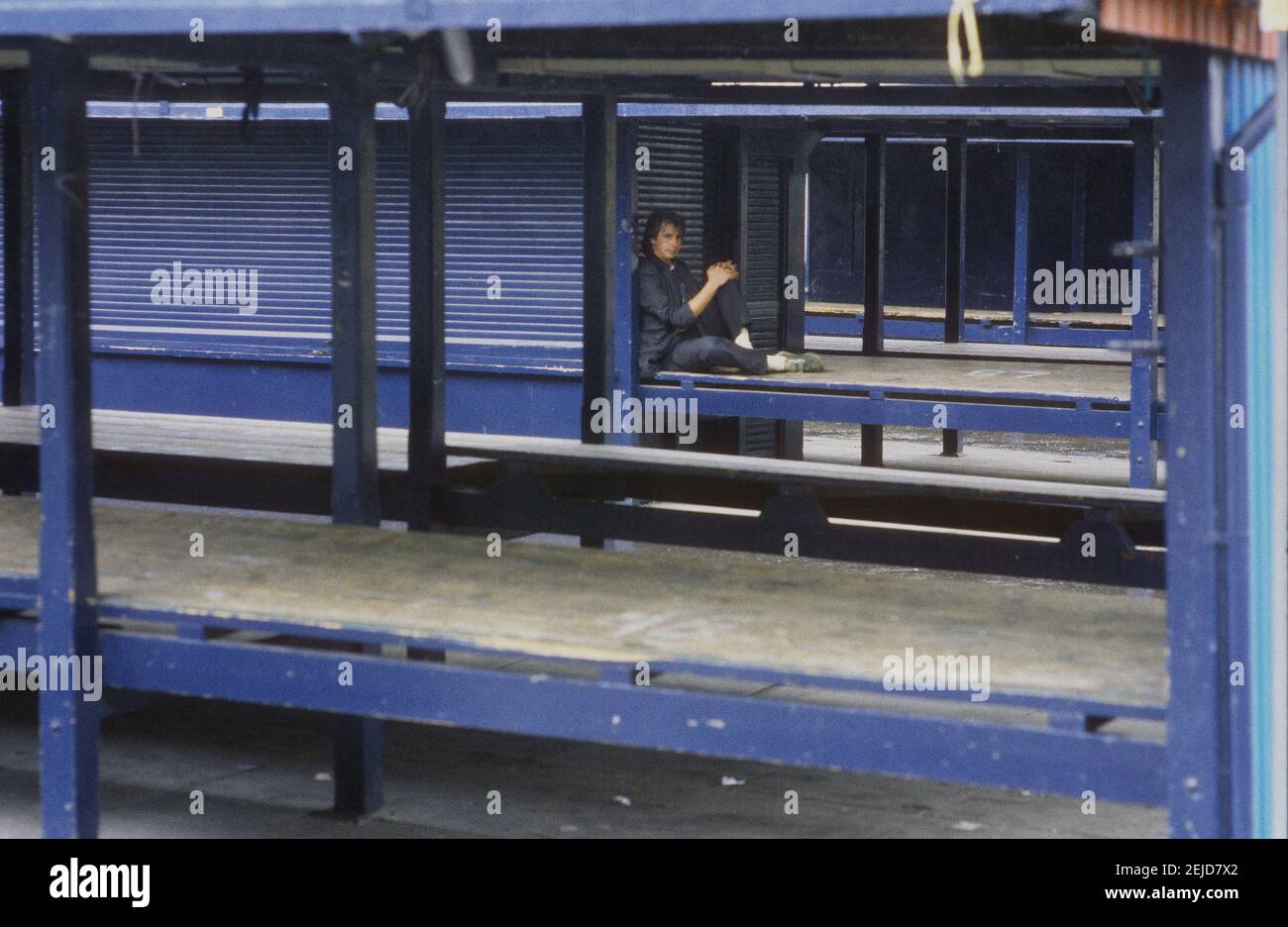 A youth sits on a stall counter to keep out of the rain on a non-market day at the Open Market in Dewsbury, Yorkshire Stock Photo