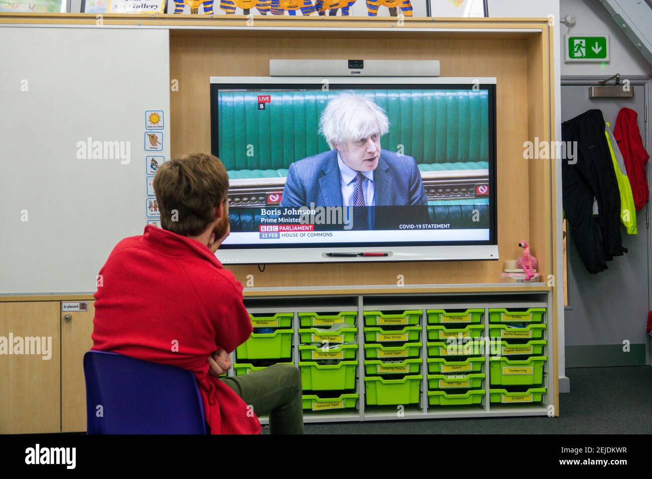 A male primary school teacher sitting in his classroom watching Prime Minister Boris Johnson on the classroom interactive smart board announce schools are to reopen to all schoolchildren in England from the 8th March. London, U.K. 22nd February, 2021. Stock Photo